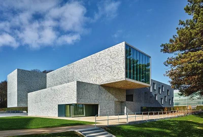 Un monolithe de béton qui affiche une présence énigmatique. le volume de la salle de danse se projette en porte-à-faux vers la citadelle de Belfort.