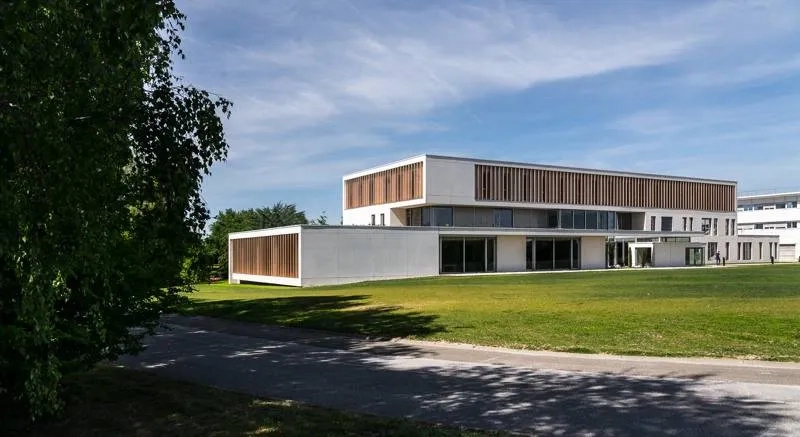 Côté sud sur la prairie, une partie du rez-de- chaussée s’étire en avant-plan, du corps vertical à R+2, dans un volume horizontal qui révèle la pente du terrain naturel et donne un socle à l’ensemble.